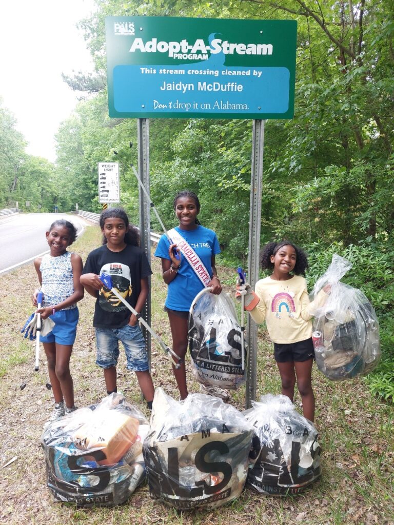Jaidyn McDuffie and friends pose next to her Adopt-A-Stream sign