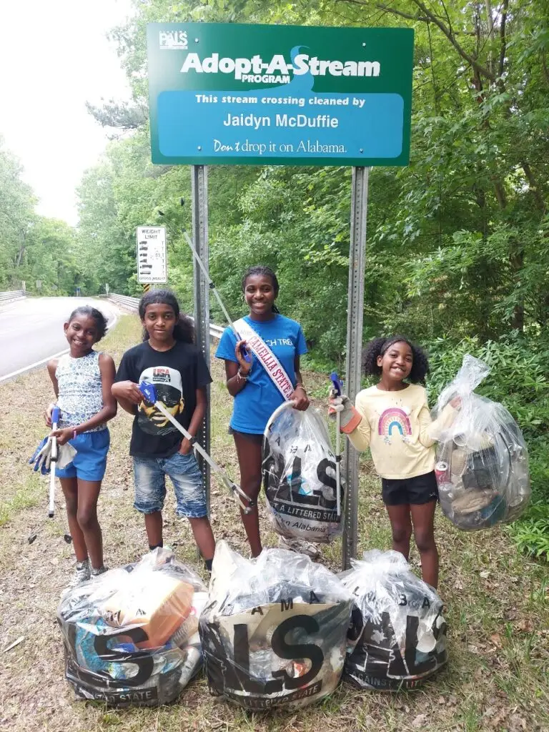 Jaidyn McDuffie and friends pose next to her Adopt-A-Stream sign